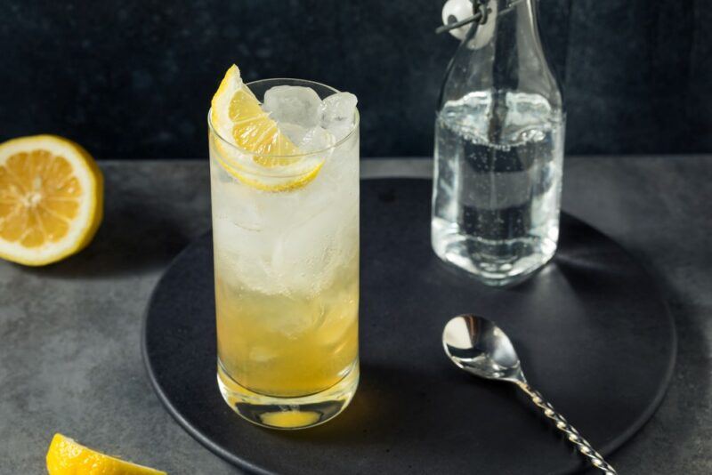 A single drambuie collins cocktail next to a lemon, bar spoon, and soda water