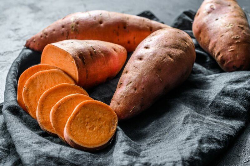 A few sweet potatoes, one of which has been cut in half and sliced