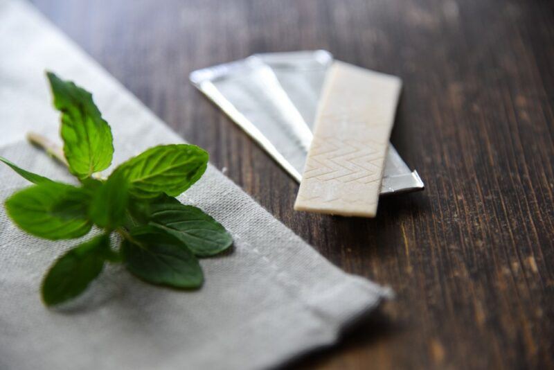 An unwrapped piece of gum on top of two wrapped ones and some stevia leaves