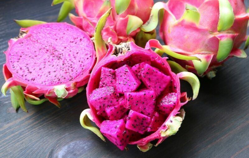 Two whole dragon fruits, one that's been cut in half and one filled with dragon fruit chunks