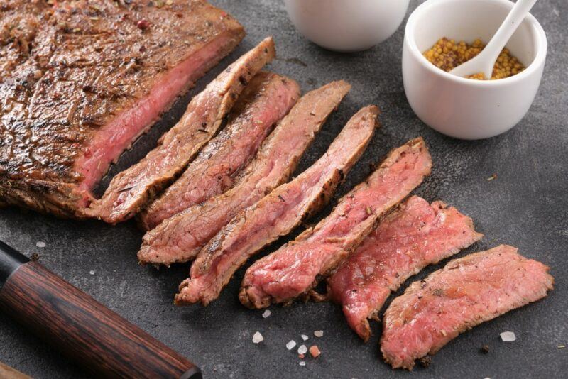 A black board with a single piece of flank steak that has been cut into thin slices