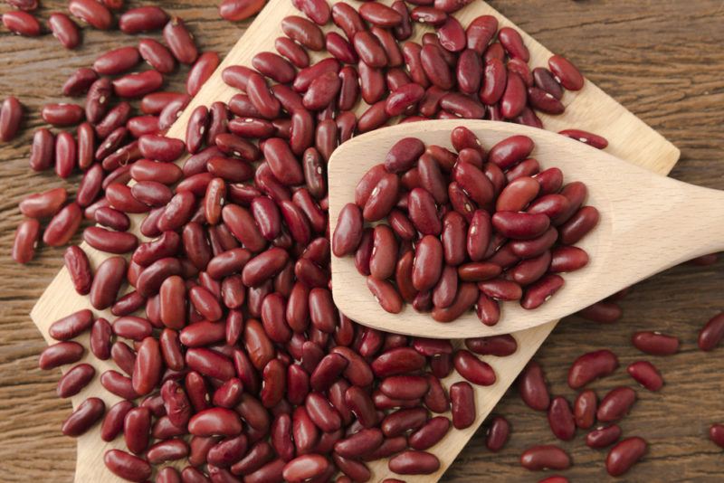 A wooden board that holds many kidney beans and more kidney beans on a wooden spoon