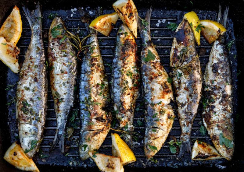 Various sardines on a dark background that have cooked, with lemons