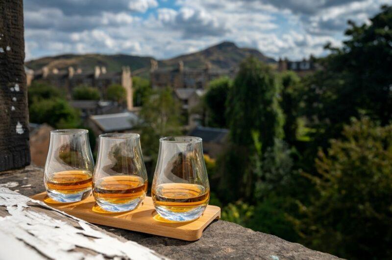 A flight of whisky glasses overlooking a view of Scotland