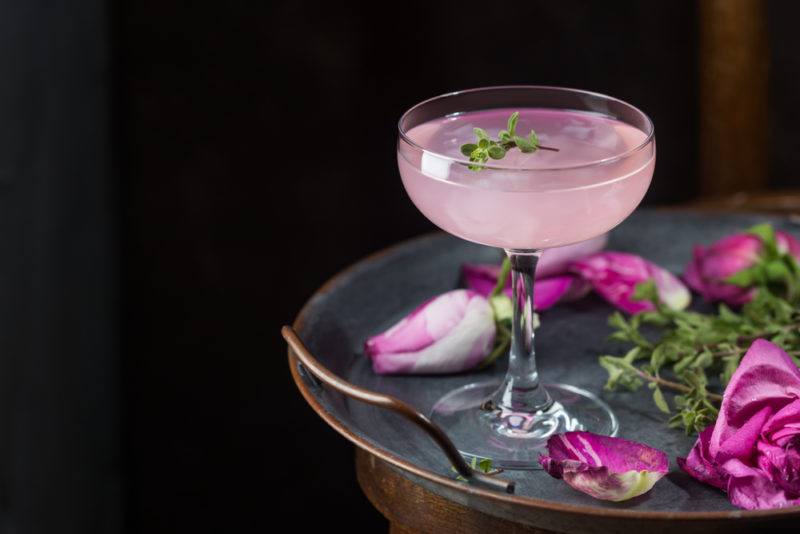 A tray with a pink mocktail and various pink flowers against a dark background