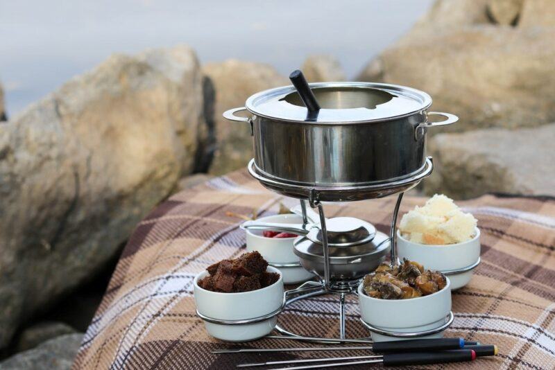 A fondue set on a picnic blanket outside with sweet ingredients surrounding it