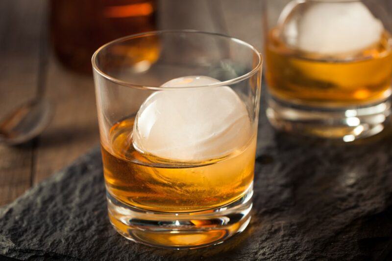 Two whiskey glasses containing a ball of ice each and a four horsemen cocktail