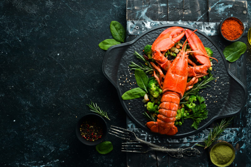 A top down image of a lobster on a bed of greens and a black tray