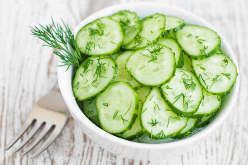 A fresh cucumber salad with dill, on a wooden table next to a fork