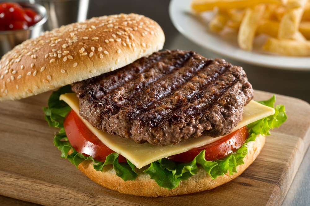 A fresh burger on a wooden board with a patty, cheese, tomato and lettuce