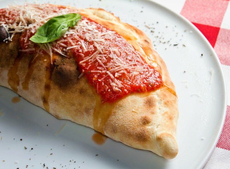 A white plate with a fried treat called a panzerotti that has some sauce and cheese on top