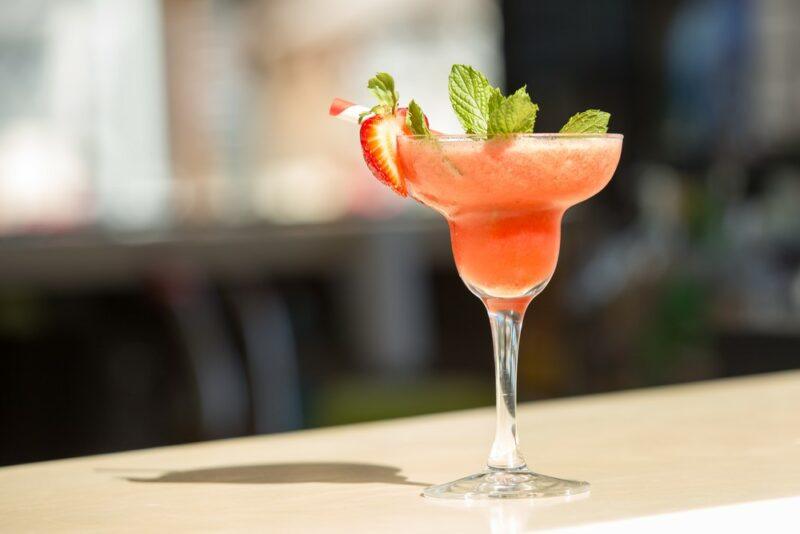 A large margarita glass containing a frozen strawberry and mango slushie, garnished with fruit and leaves