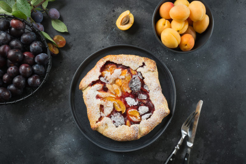 A fruit galette on a black table next to some pieces of fruit