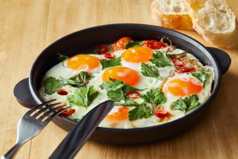 A black fry pan with multiple eggs and some greens for breakfast