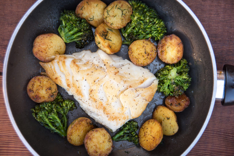 A black frypan with roast potatoes and broccoli