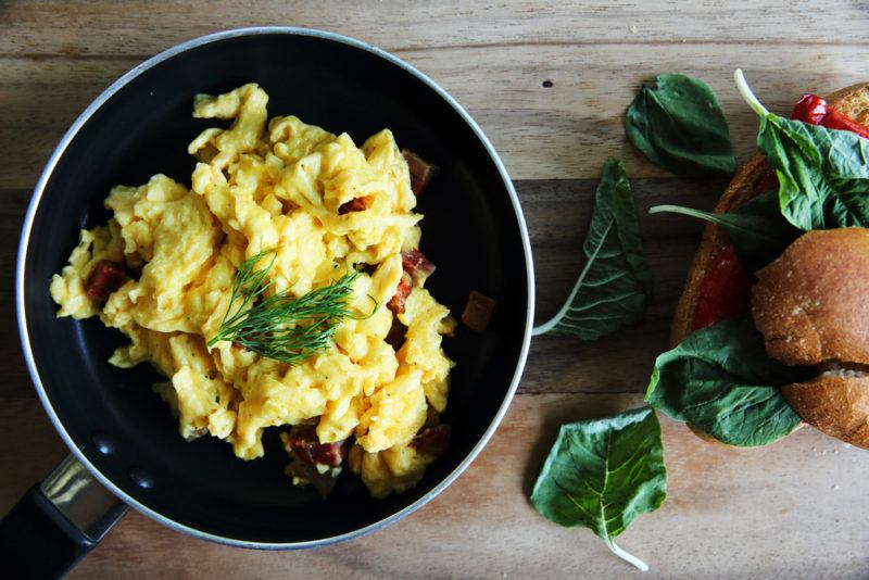 A black frypan that contains scrambled eggs, next to some greens