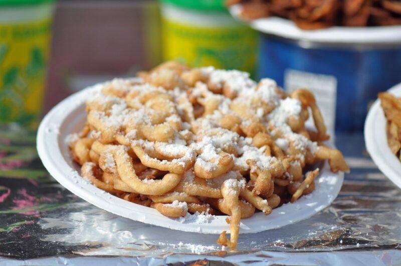 A white plate containing a fair food called funnel cake, which has been topped with powdered sugar