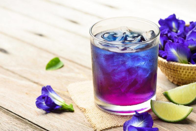 A galaxy cocktail in a glass next to pea flowers and lime wedges