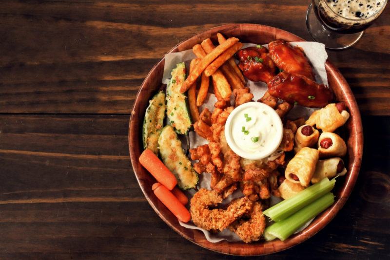 A game day platter that includes jalapeno poppers, along with celery, dip, pigs in a blanket, and fried food