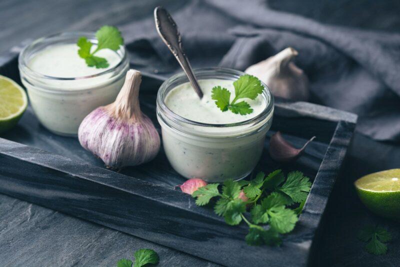 A dark slate with two bowls of garlic, lime and cilantro dip, with a head of garlic in the middle