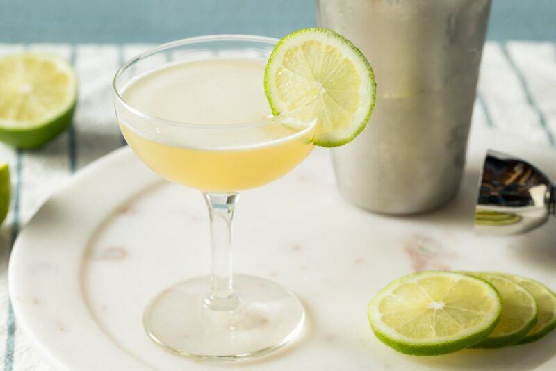 A tray with a gimlet cocktail, limes, and a cocktail shaker