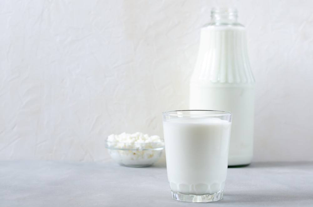 A glass dish of milk kefir grains, with a bottle and a glass of milk kefir