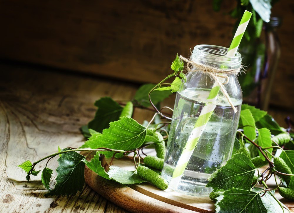 A glass bottle of birch juice next to leaves