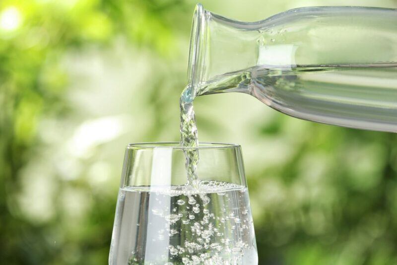 A glass of mineral water being poured from a bottle, in front of leaves