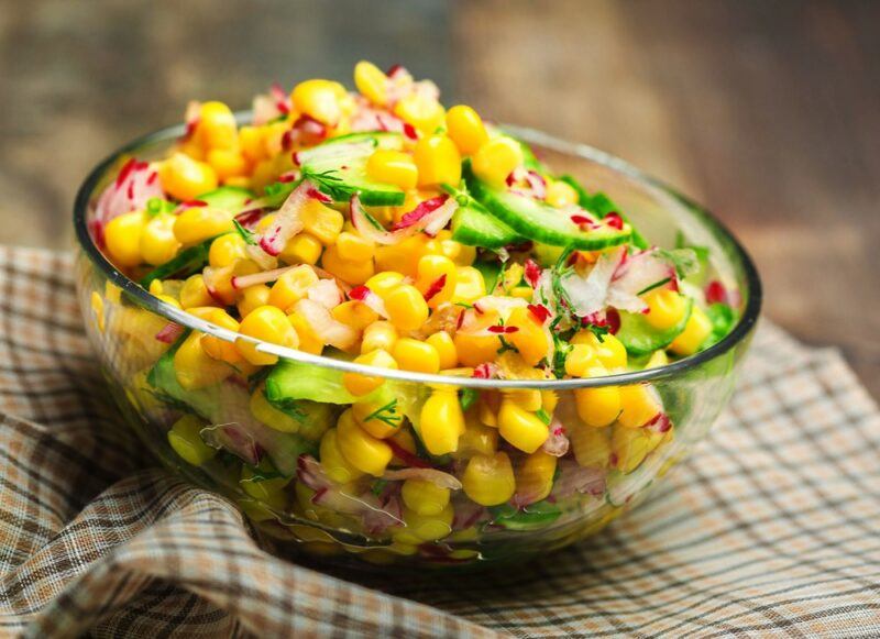 A glass bowl filled with a corn salad for a picnic or summer event