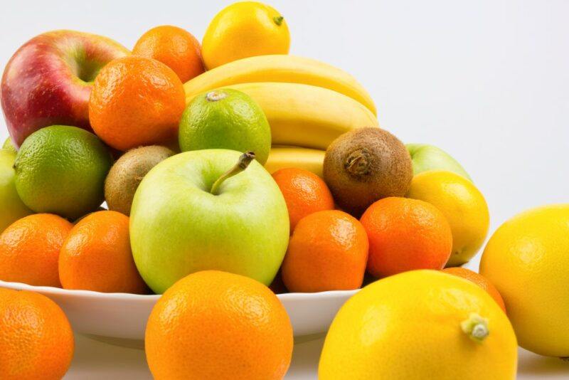 A white plate with many different pieces of fresh fruit, including bananas, apples, and oranges