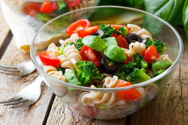 A large glass bowl with a pasta salad containing broccoli, pasta, and peppers