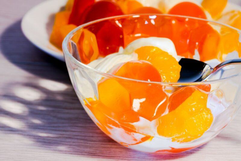 A glass bowl containing a dessert made using orange jello and cream