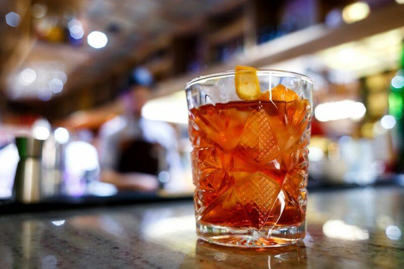 A glass containing a Cuban sarsaparilla cocktail on a table, with an out of focus bar in the background