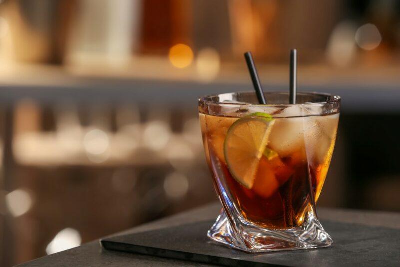 A glass of a Guinness black magic cocktail with two straws in front of an out of focus bar