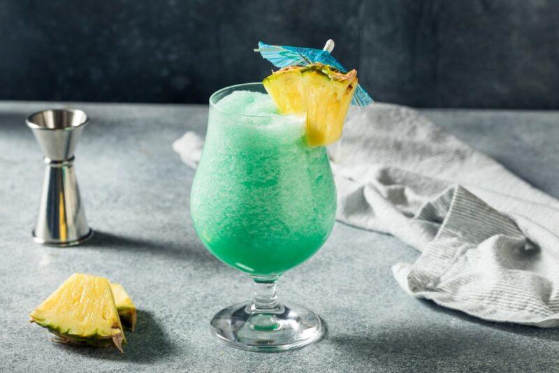 A slushie style drink called a blue Hawaiian on a bar next to lemon and a jigger