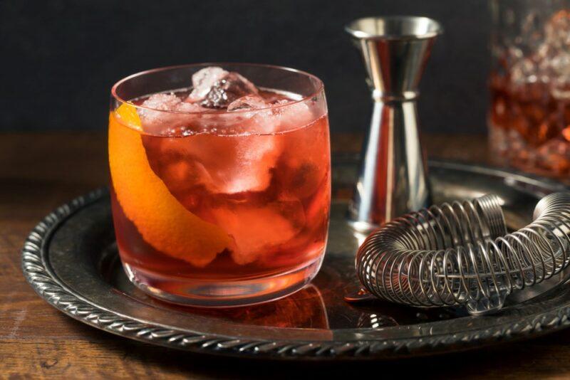 A silver tray with a boulevardier cocktail next to a cocktail strainer and a cocktail jigger