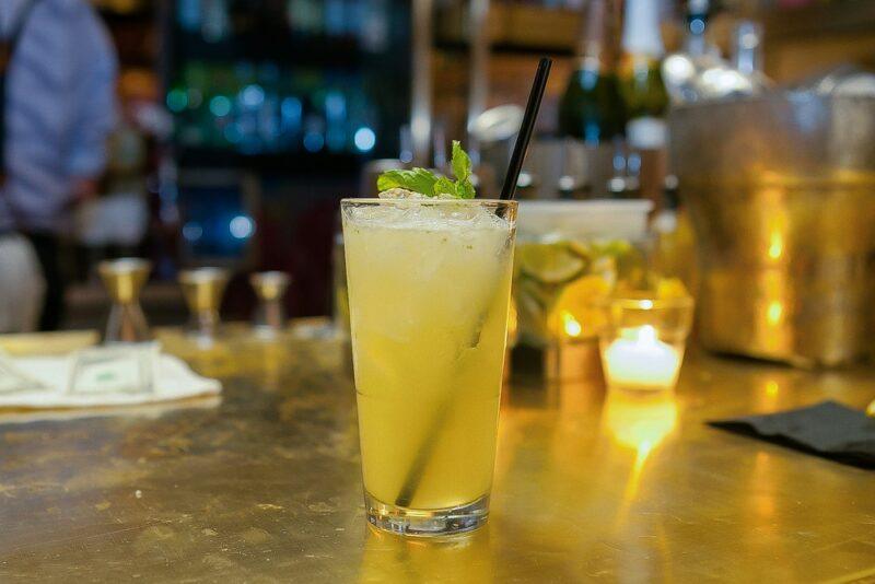 A tall glass with a straw on a bar, containing a bull bee cocktail