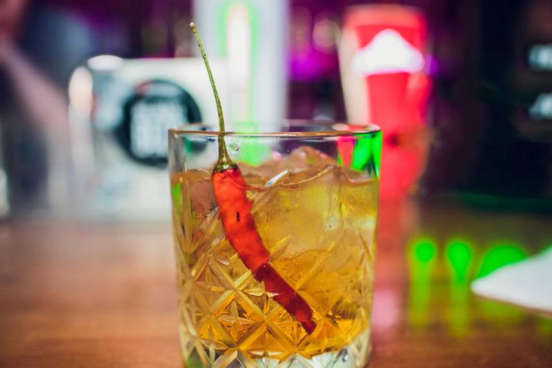 A cocktail in a glass with a chili pepper as a garnish