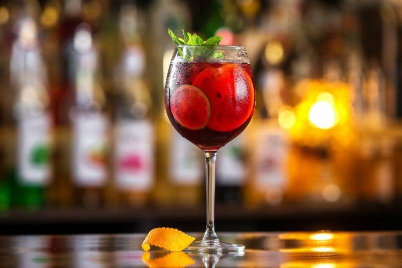 A tall glass containing a honey cobbler cocktail in front of an out of focus bar