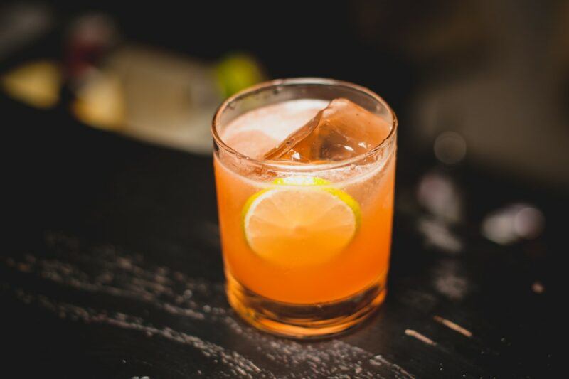 A single glass containing a man o' war cocktail on a black or brown table