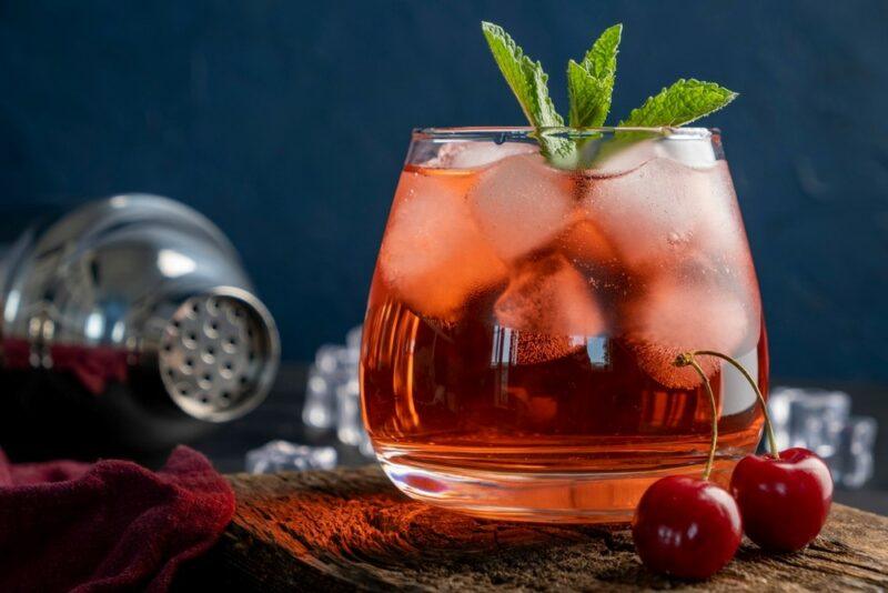 A glass filled with a peanut butter and jelly cocktail with plenty of ice, next to a cocktail shaker