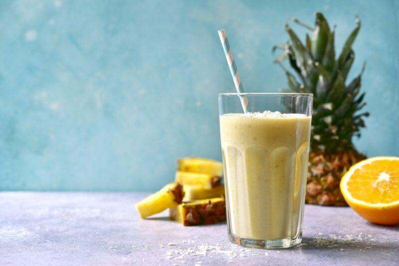 A tall glass containing a pineapple batida cocktail, next to pineapple wedges