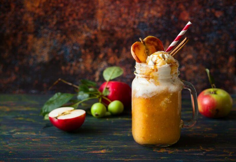 A glass mason jar with an apple pie whiskey float and straws on a table with fresh apples as well