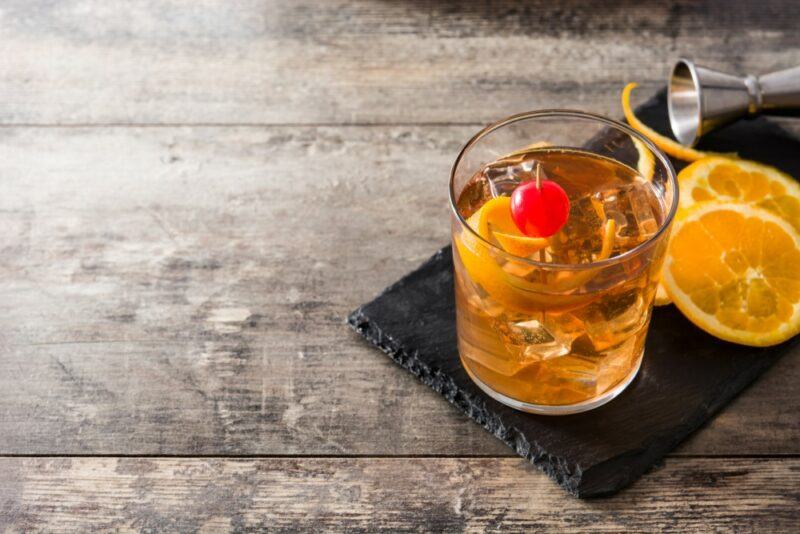 A glass containing an old fashioned cocktail with ice, next to two lemon slices