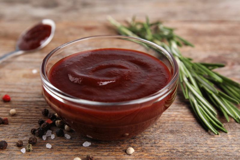 A glass bowl of BBQ sauce next to sprigs of herbs