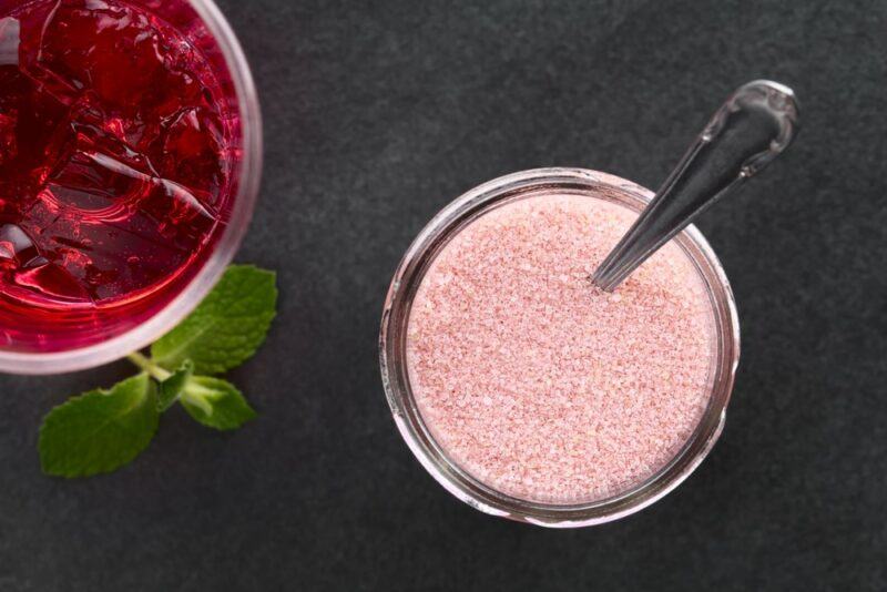 A small glass dish of jello powder with a spoon, next to a container of prepared red jello