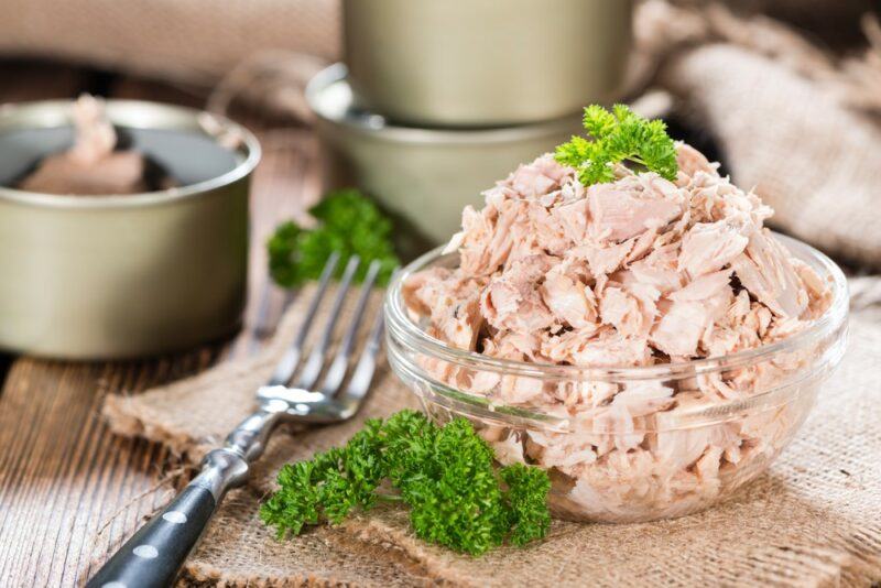 A glass dish of tuna, next to three cans of tuna and a fork