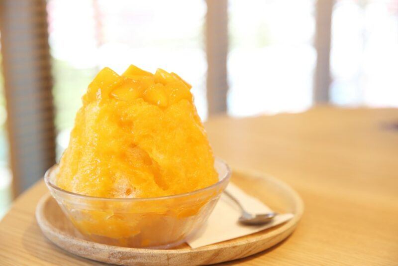 A glass dish with a tall fuzzy navel snow cone next to a spoon