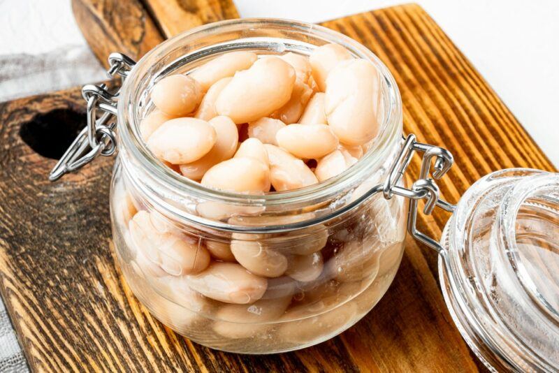 A glass jar filled with cooked white beans on a wooden board