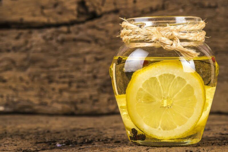 A wooden table and wall with a jar of olive oil and a slice of lemon